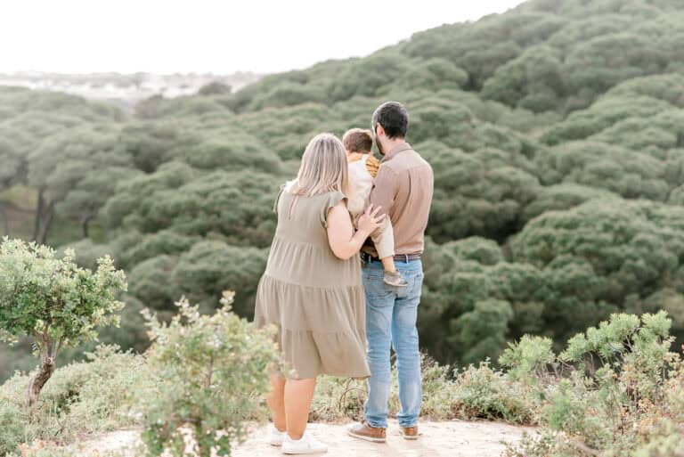 Casal com uma criança ao colo, vistos de costas, a apreciar uma paisagem natural repleta de árvores.