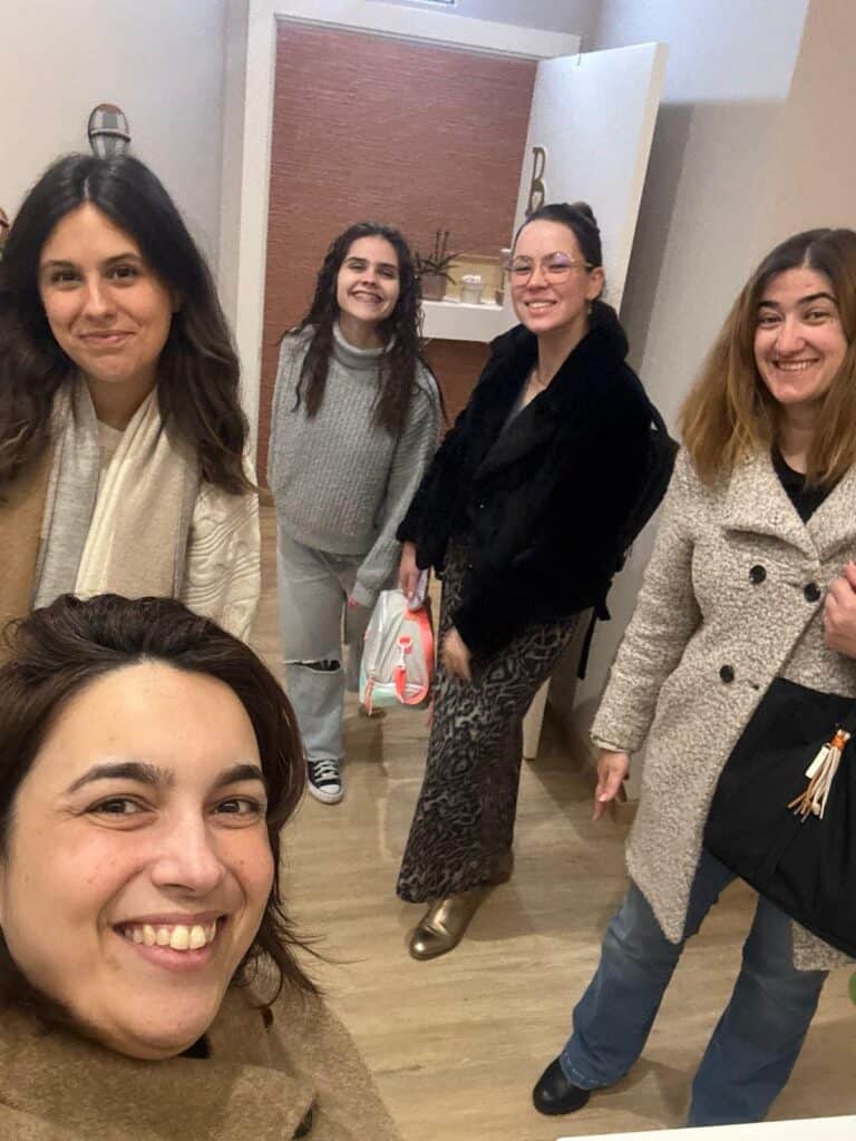 Close-up selfie of a woman in a tan coat with four friends smiling in a clothing boutique