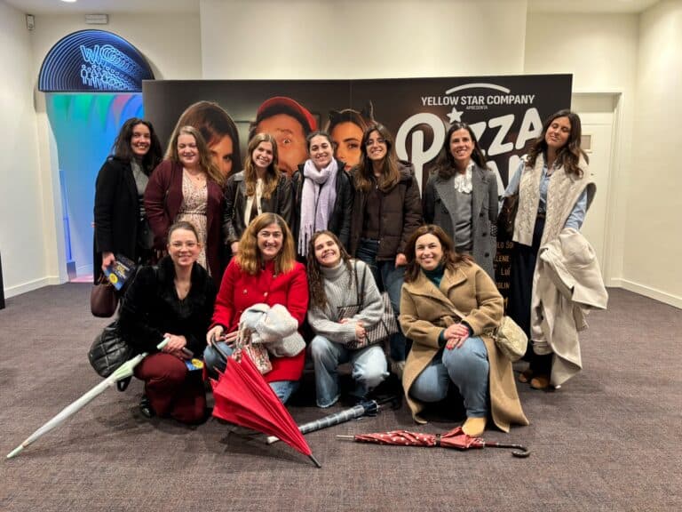 Group of smiling women posing indoors in front of a black banner with 'Yellow Star Company' text; several umbrellas lie on the carpeted floor in front of them.